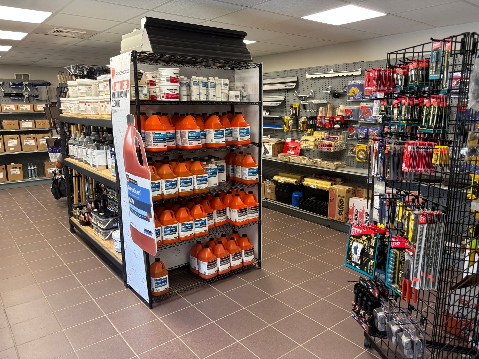 Retail store aisle with shelves of tools and orange packaged supplies under bright fluorescent lights