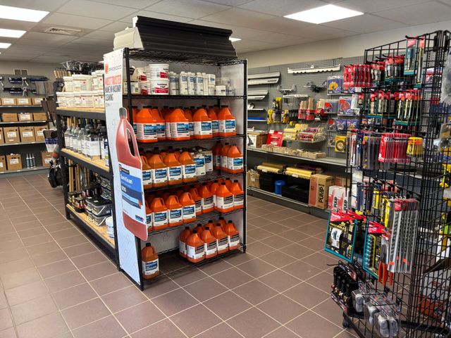 A store aisle with shelves of packaged snacks, drinks, and hardware items under bright fluorescent lights.