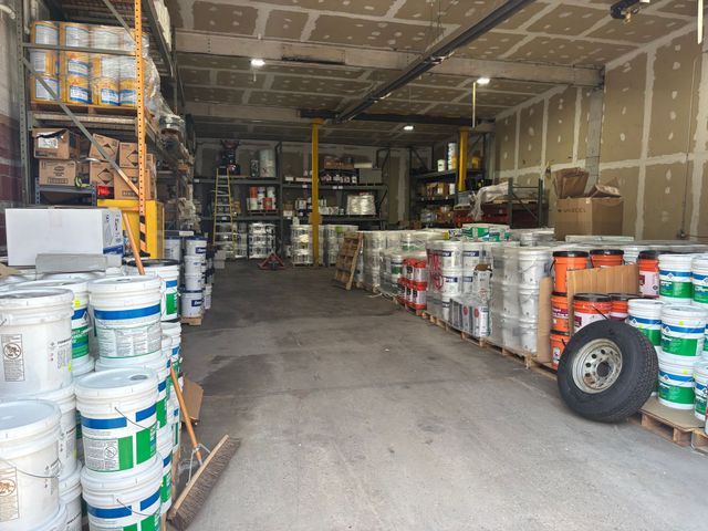 Warehouse aisle filled with stacked paint buckets and supplies on both sides