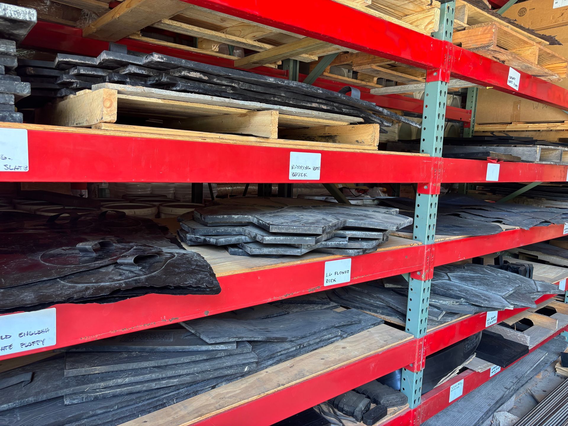 Shelves of stacked dark fabric or material rolls on red industrial racking in a warehouse