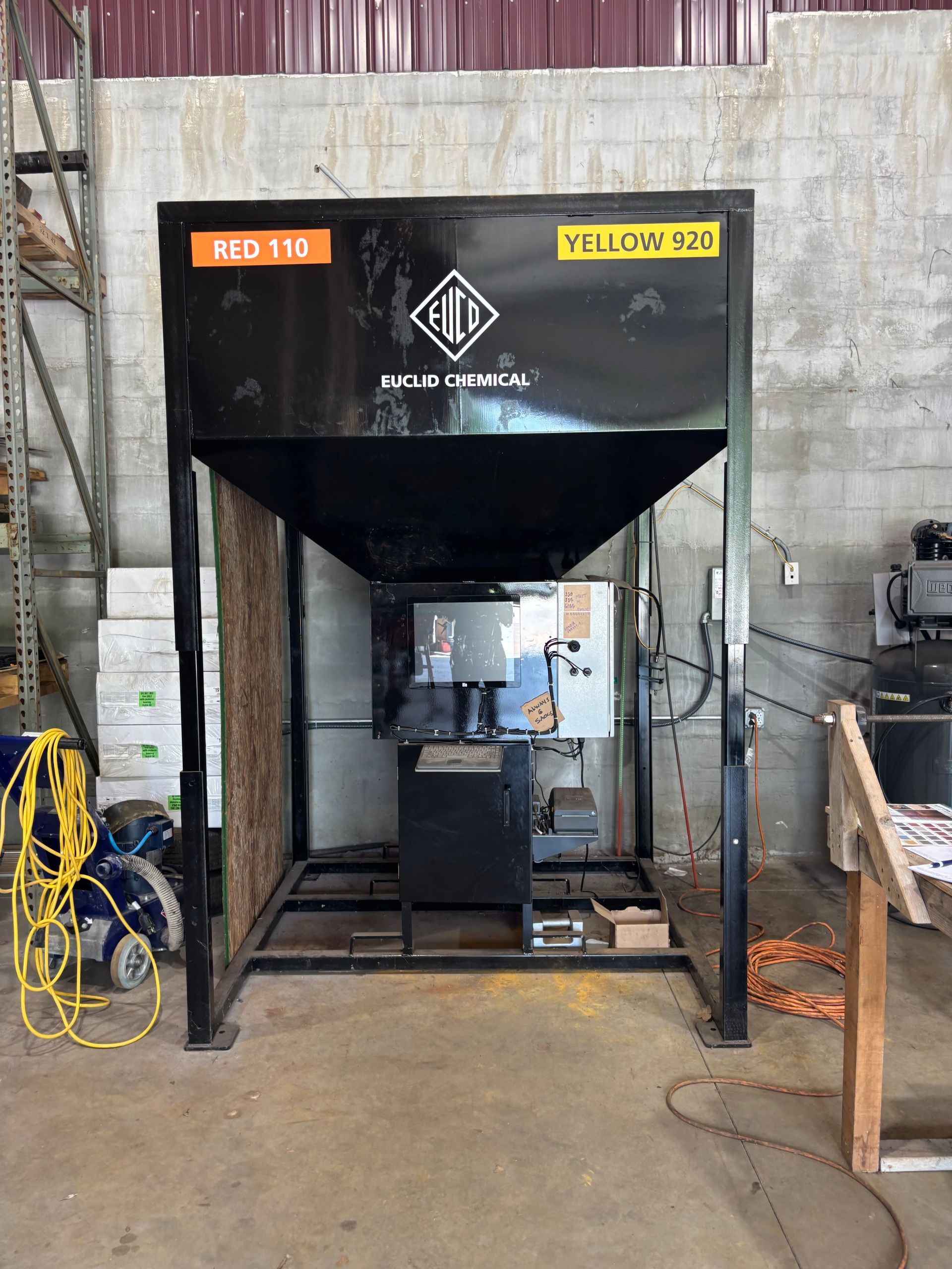 Industrial machine in a warehouse, black hopper with a metal frame and control panel.