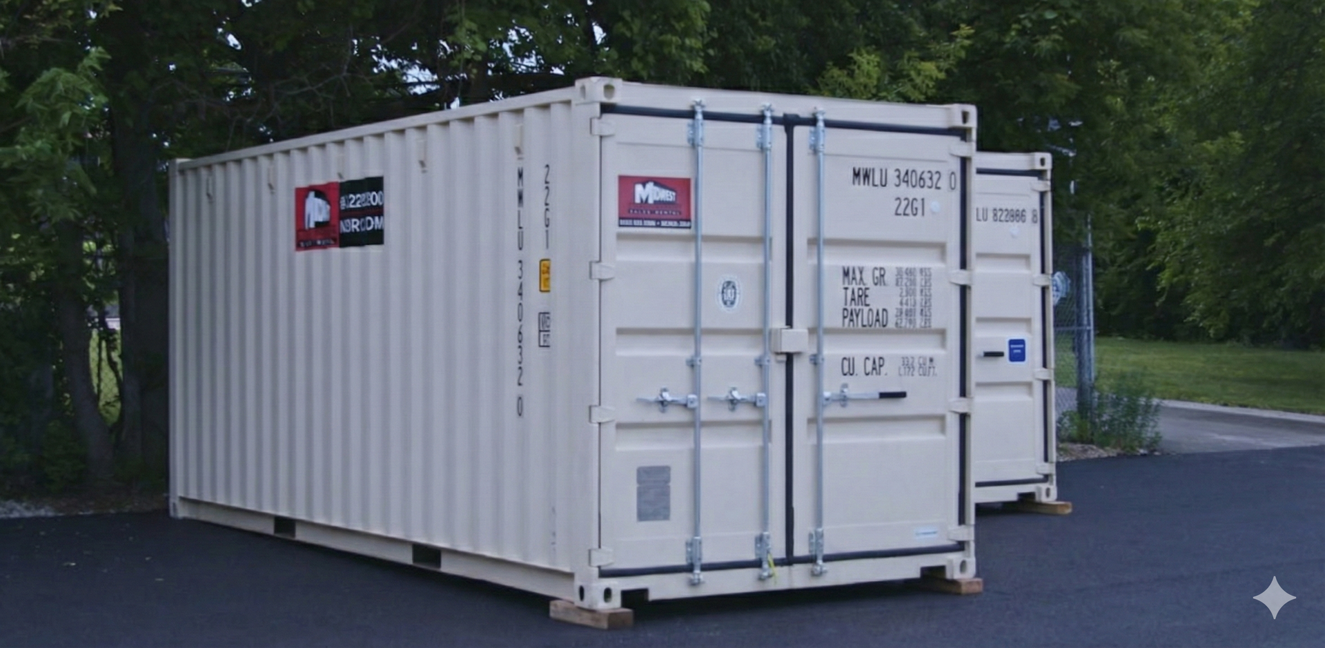 Two white shipping containers in a parking lot, near green trees.