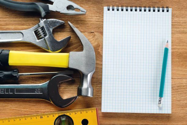 Assorted hand tools and a notepad with pencil on a wooden workbench