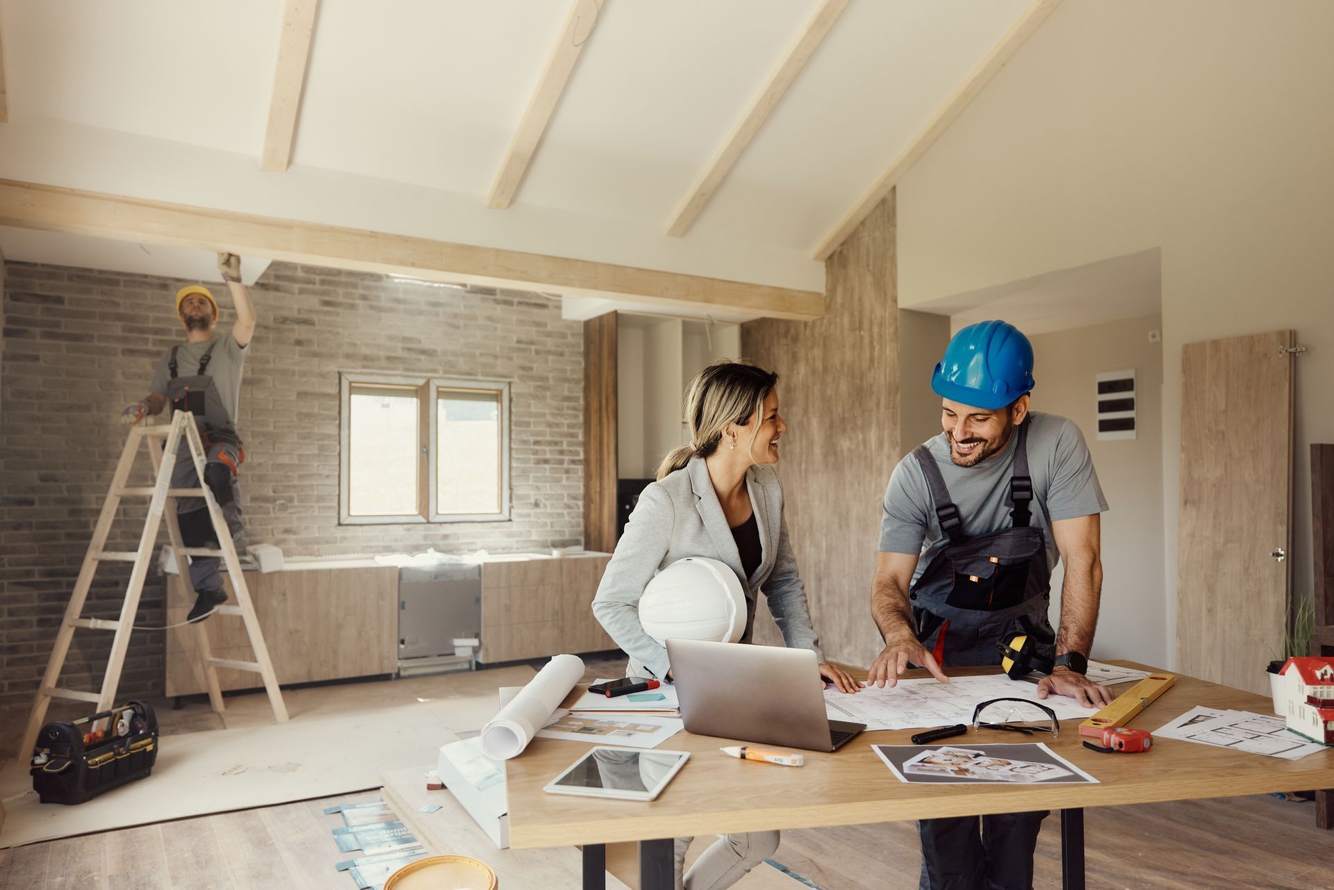 Two workers reviewing plans at a construction site renovation, with ladders, tools, and debris around them
