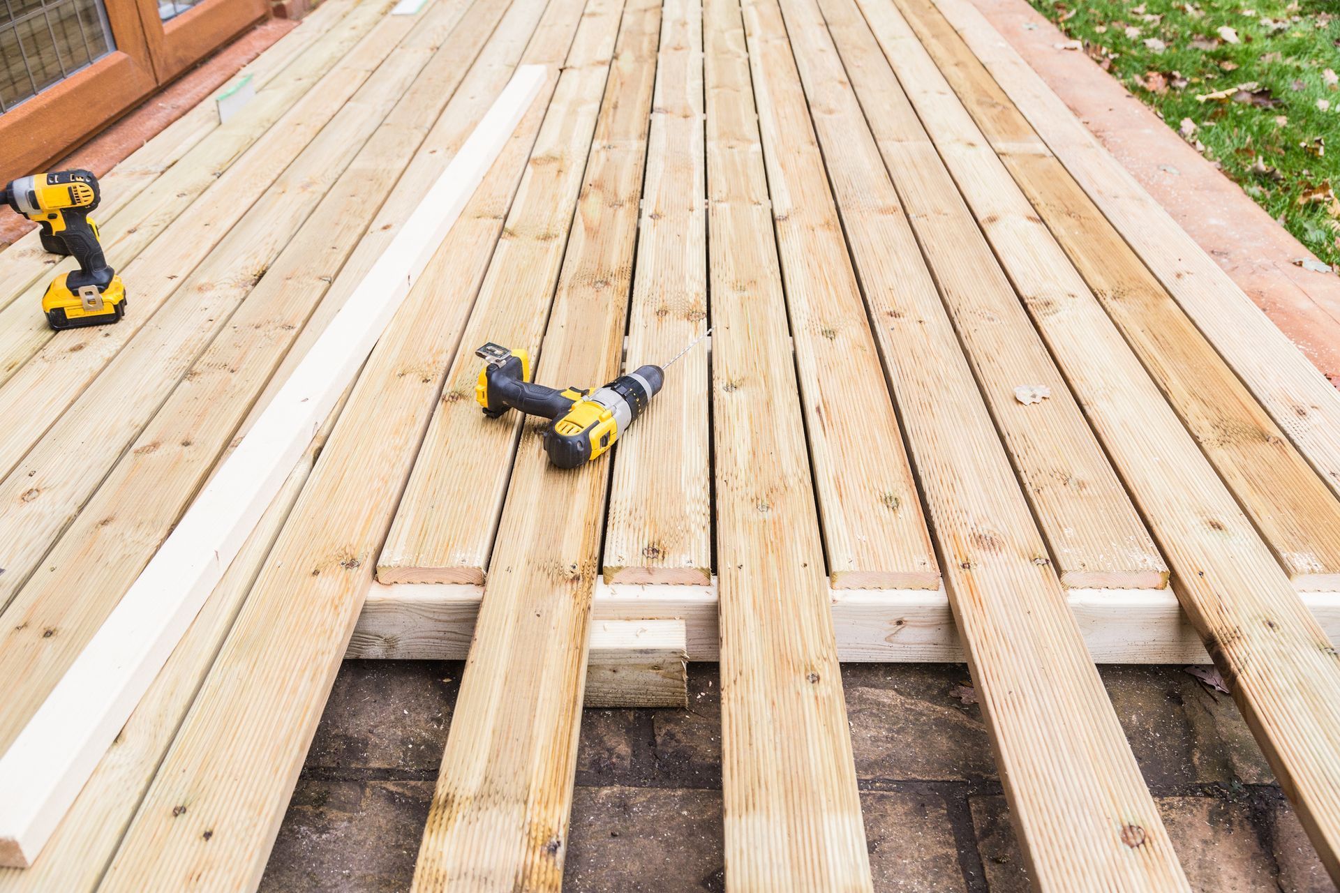 Wooden deck framing under construction with two yellow cordless drills on the planks
