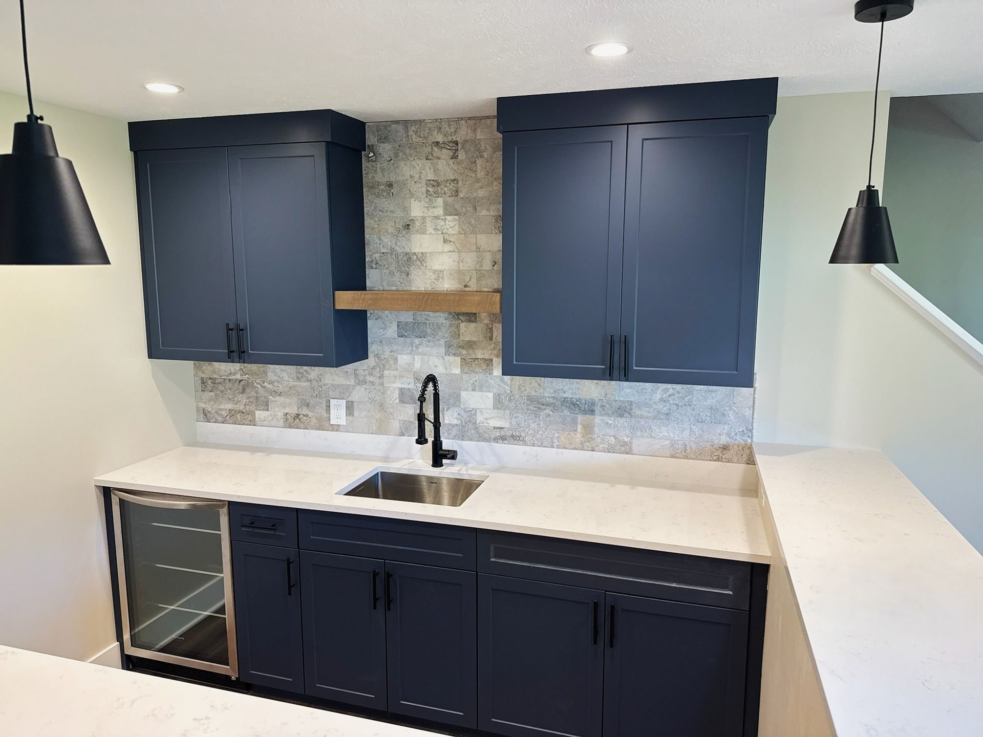 Modern kitchen with dark blue cabinets, white countertops, a sink, and hanging black pendant lights.
