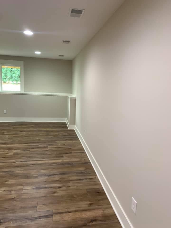 Empty basement room with gray walls, wood-look flooring, recessed lights, and a small window.