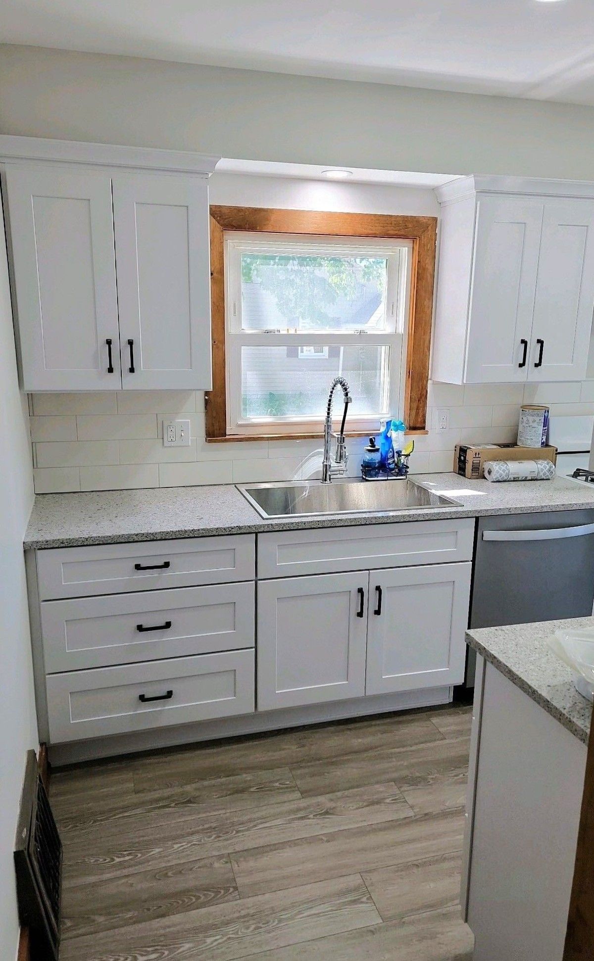 Bright white kitchen with sink under window, gray counters, white cabinets, and wood-look flooring