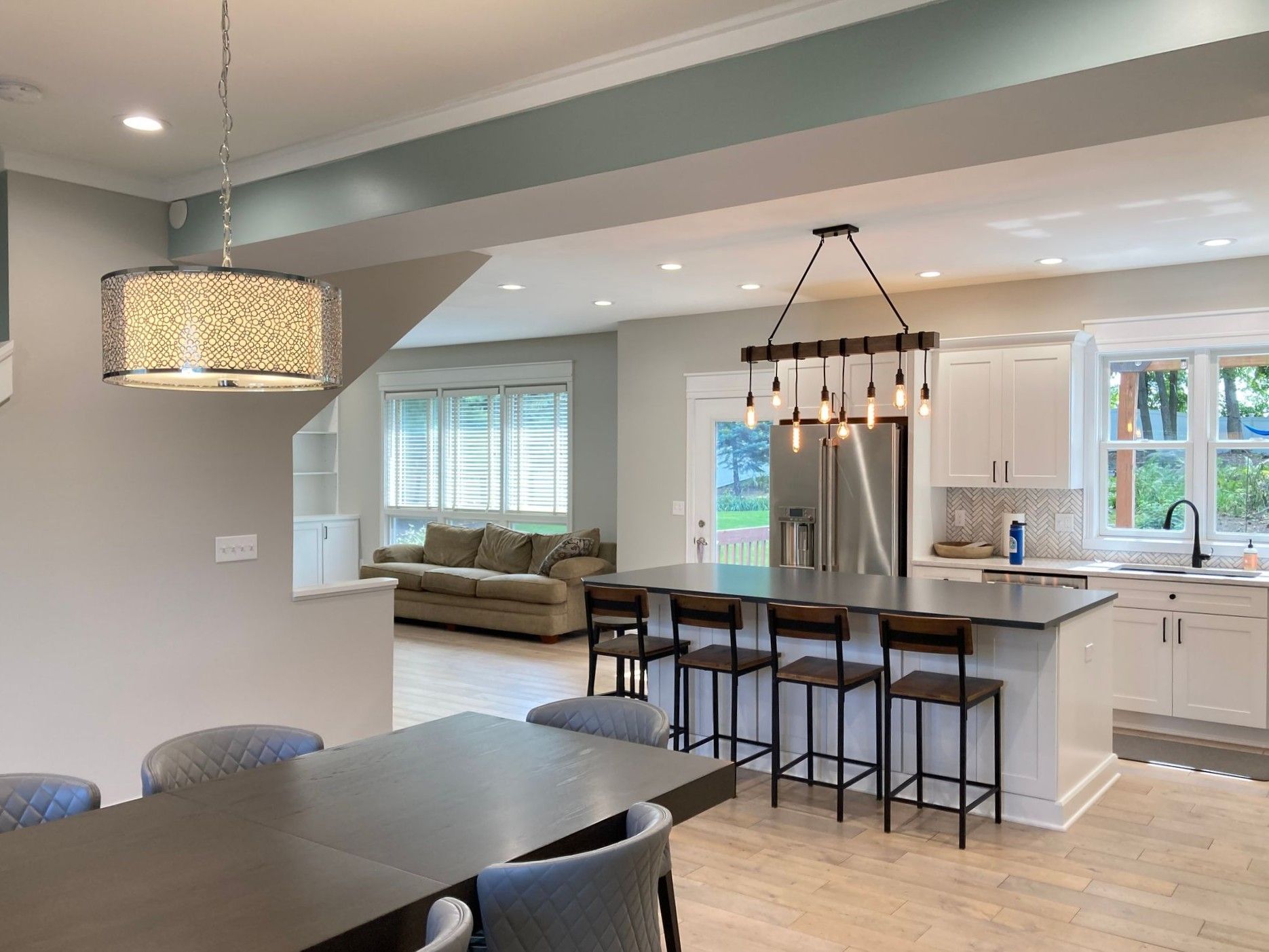 Open-plan kitchen and living room with island, pendant lights, white cabinets, and gray dining table
