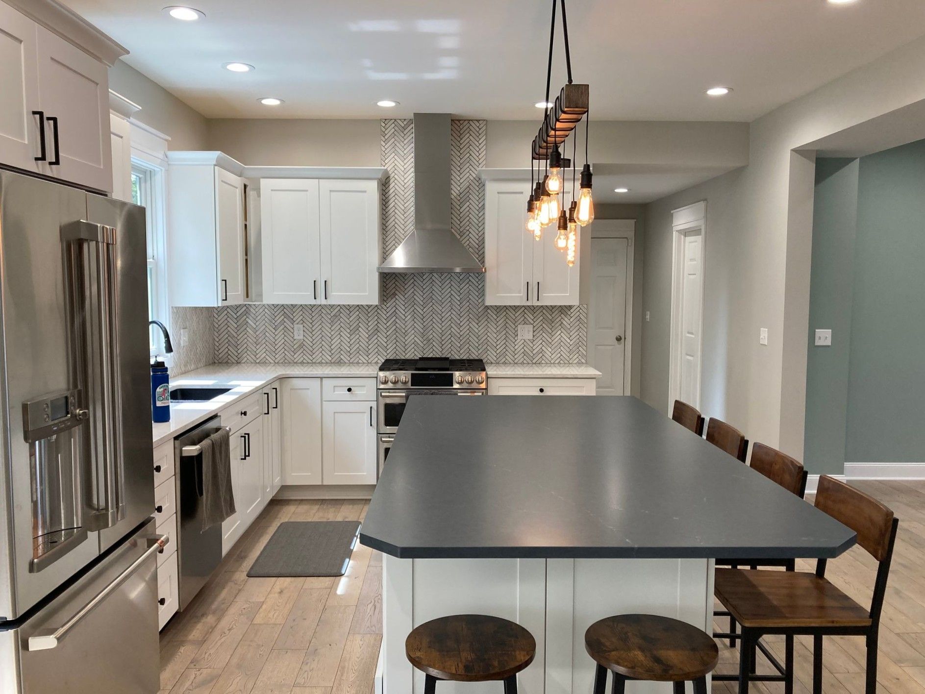 Modern kitchen with white cabinets, gray island, stainless fridge, and pendant lights