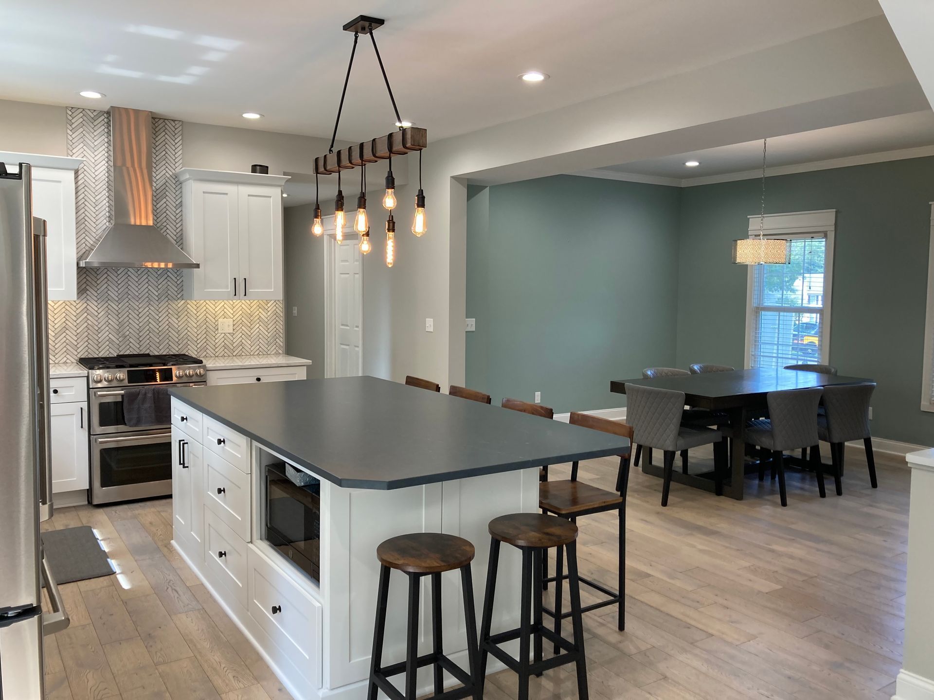 Modern kitchen with gray island, pendant lights, and open dining area in the background