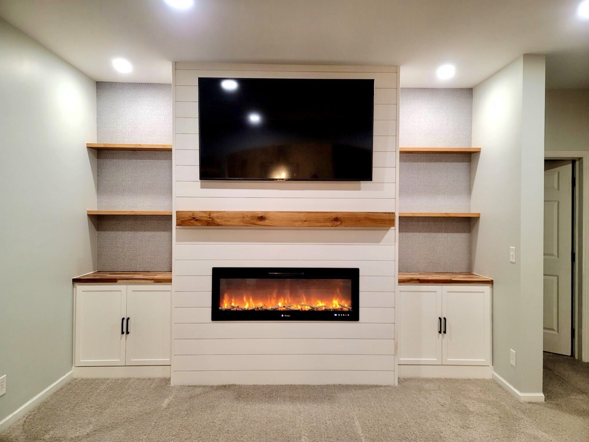 Modern living room built-in entertainment wall with TV, electric fireplace, shelves, and cabinets