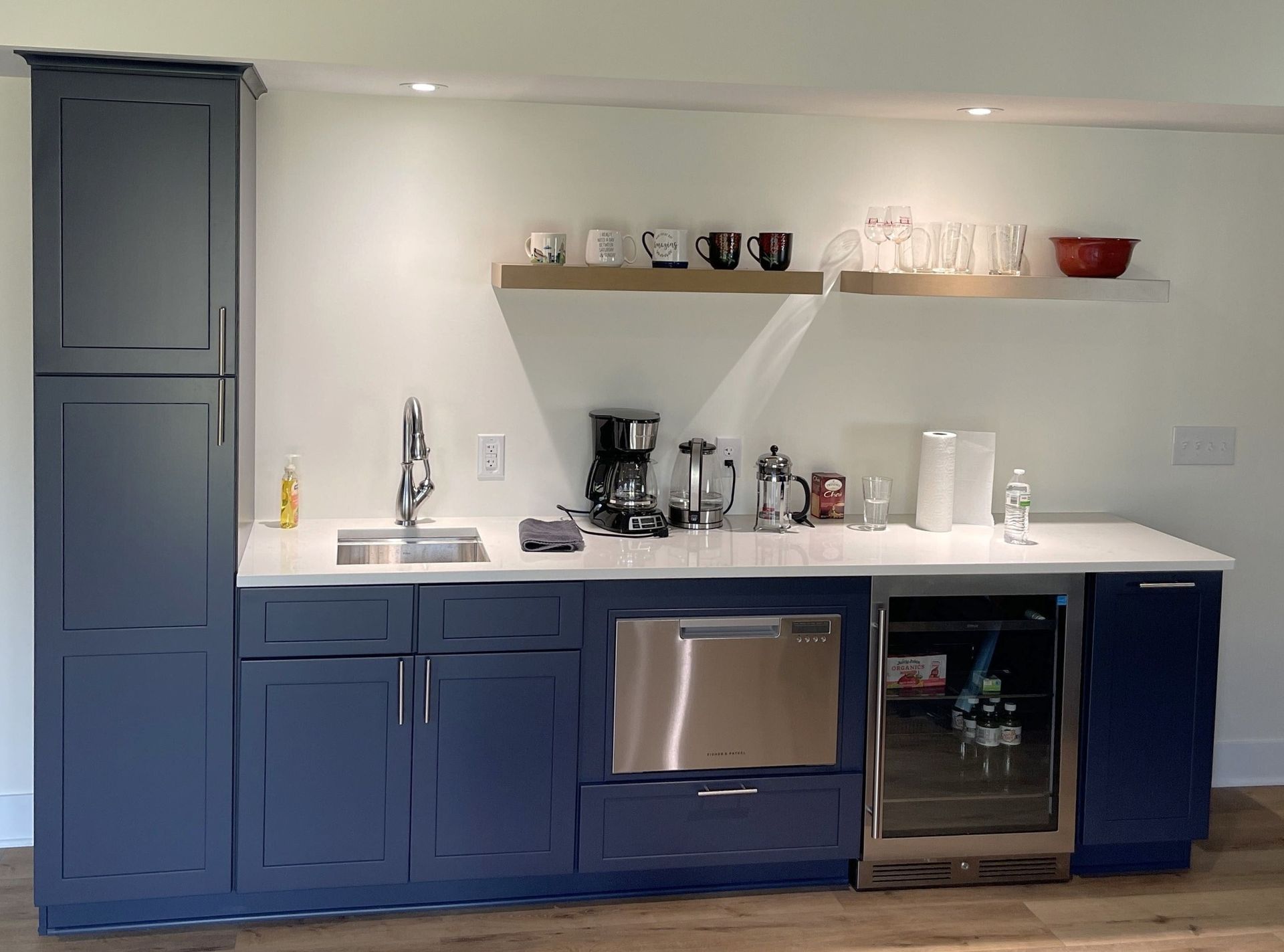 Blue kitchen kitchenette with sink, coffee maker, shelves, and stainless-steel mini fridge under counter