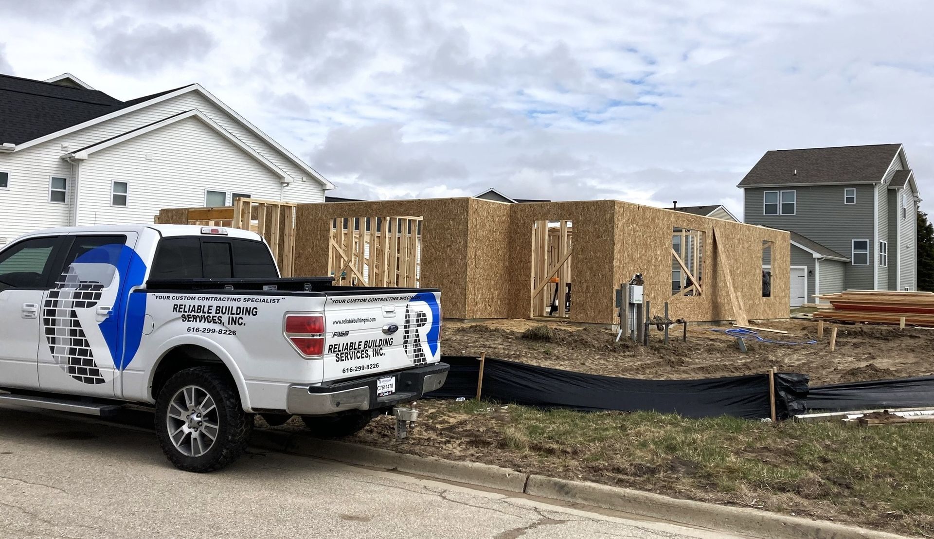 White pickup truck parked by a house under construction with wooden framing and wrapped siding nearby