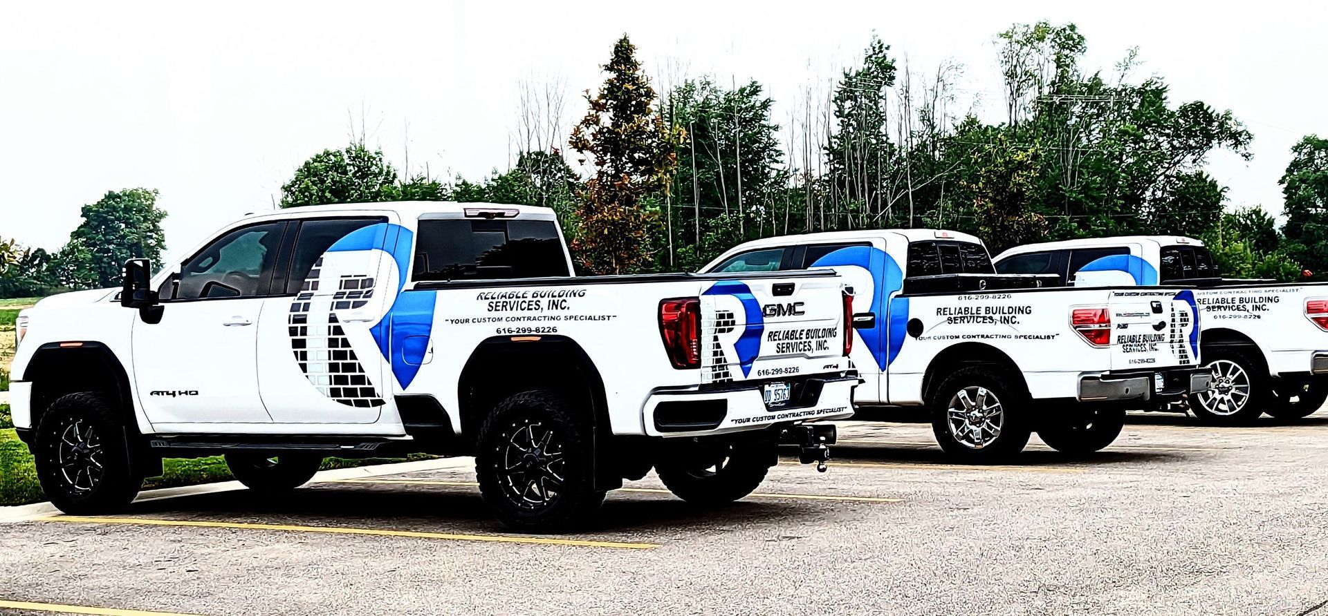 Three white pickup trucks with blue graphics parked in a row on gravel outdoors