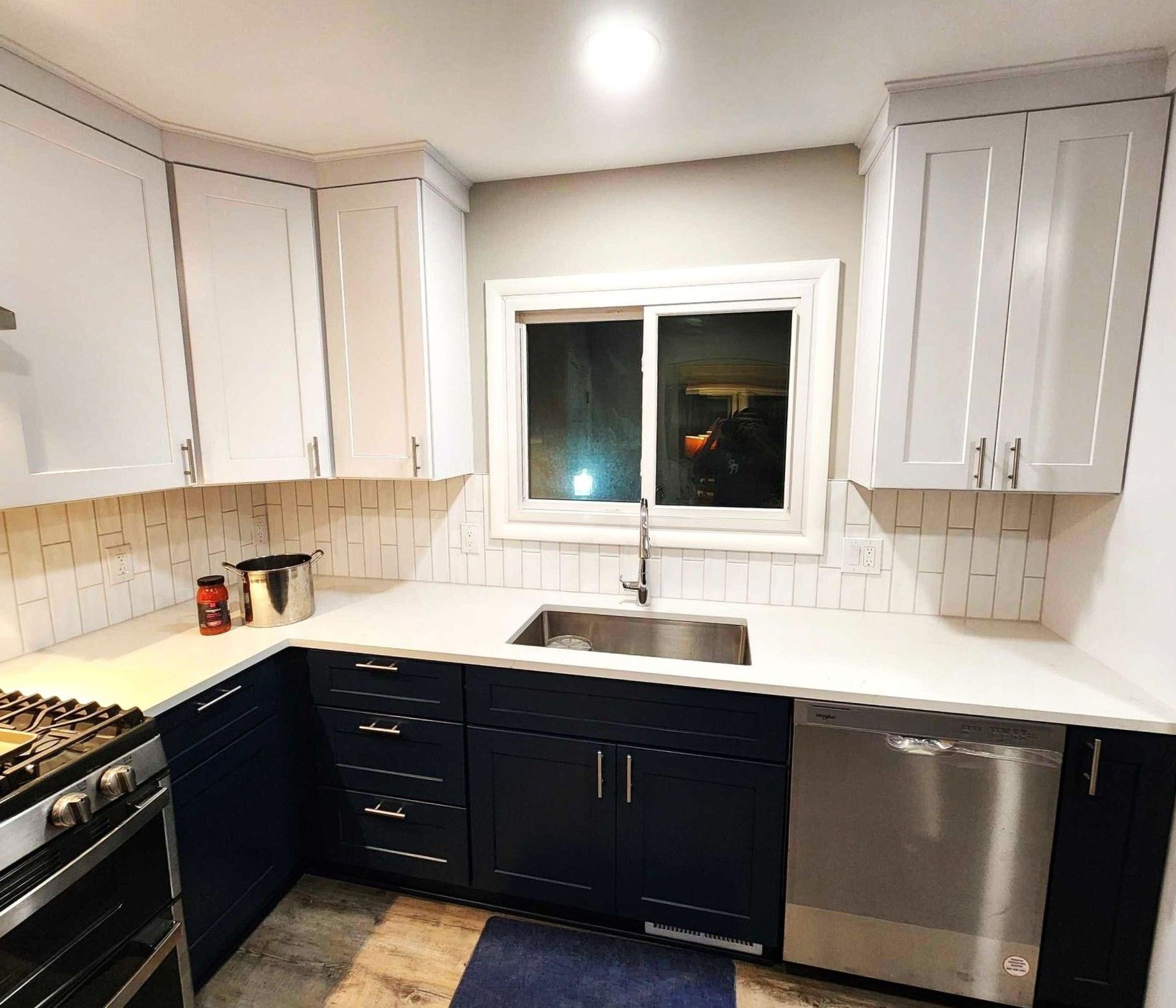 Modern kitchen with white cabinets, dark lower cabinets, stainless dishwasher, sink, and white countertops.