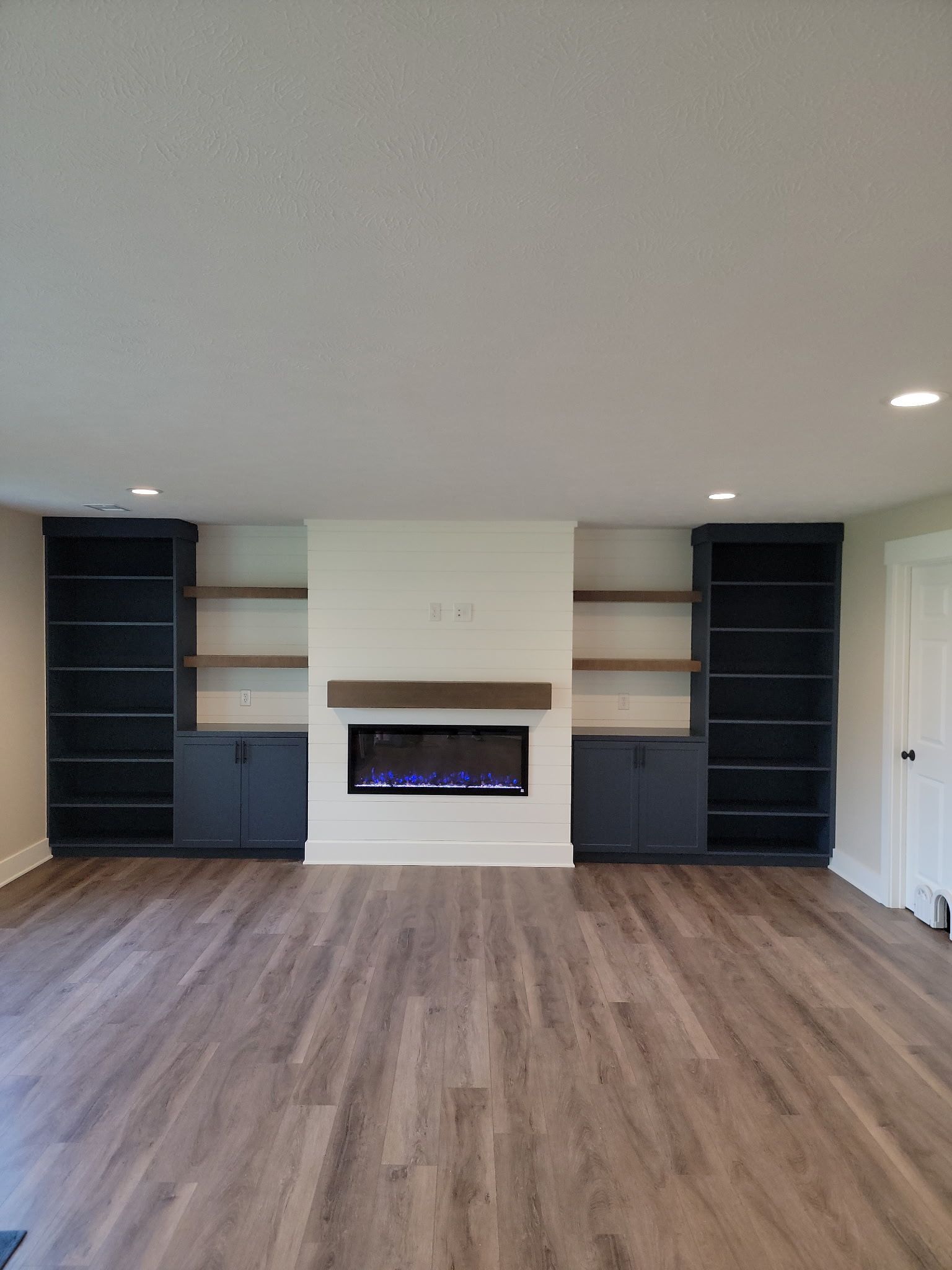 Empty living room with built-in shelving and a modern fireplace, dark wood flooring, and recessed lighting.