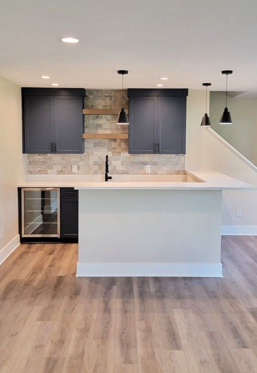 Modern kitchen with navy cabinets, white island, pendant lights, and wood flooring.