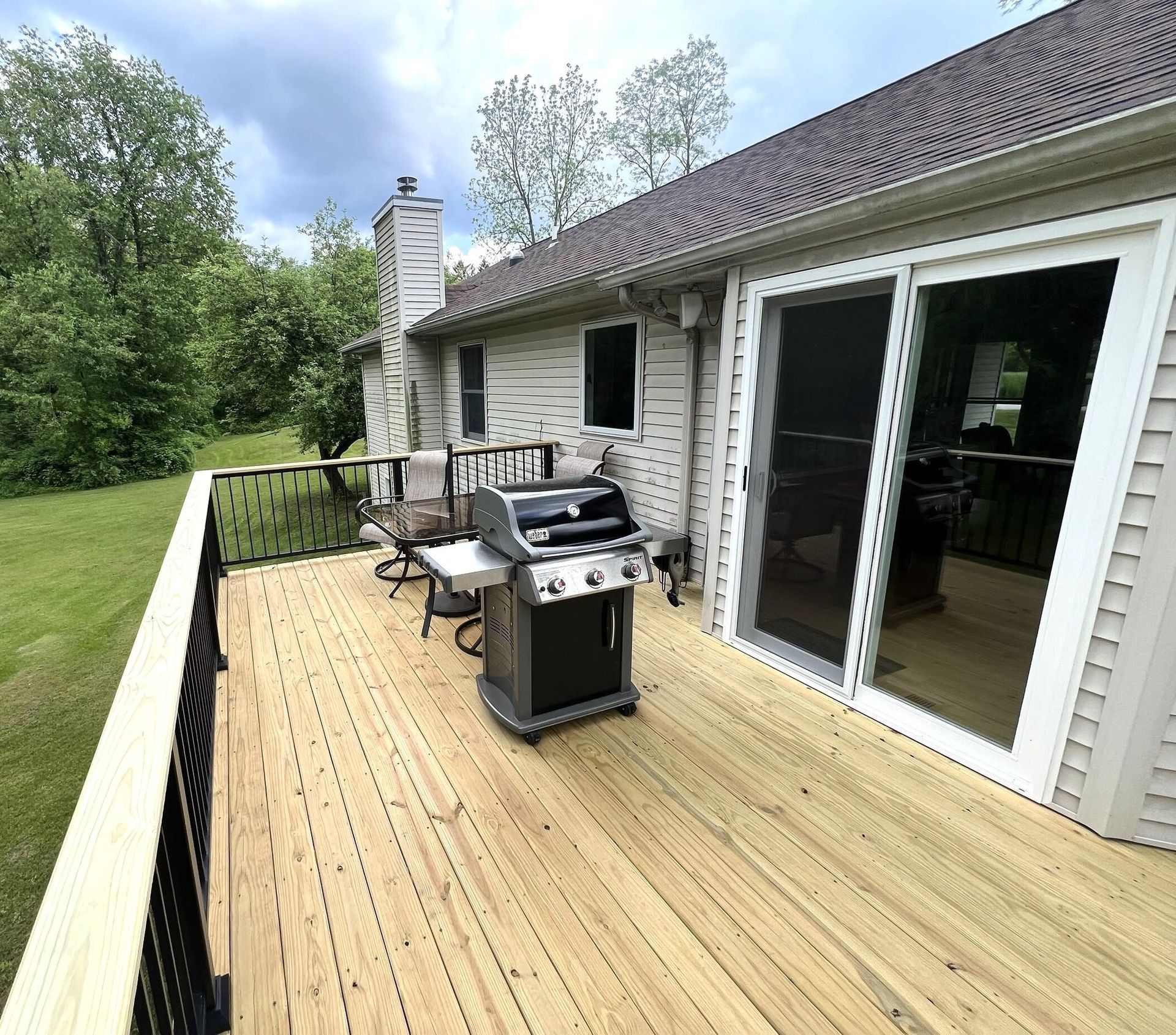 Wooden backyard deck with black railing, grill, and sliding glass doors beside a house