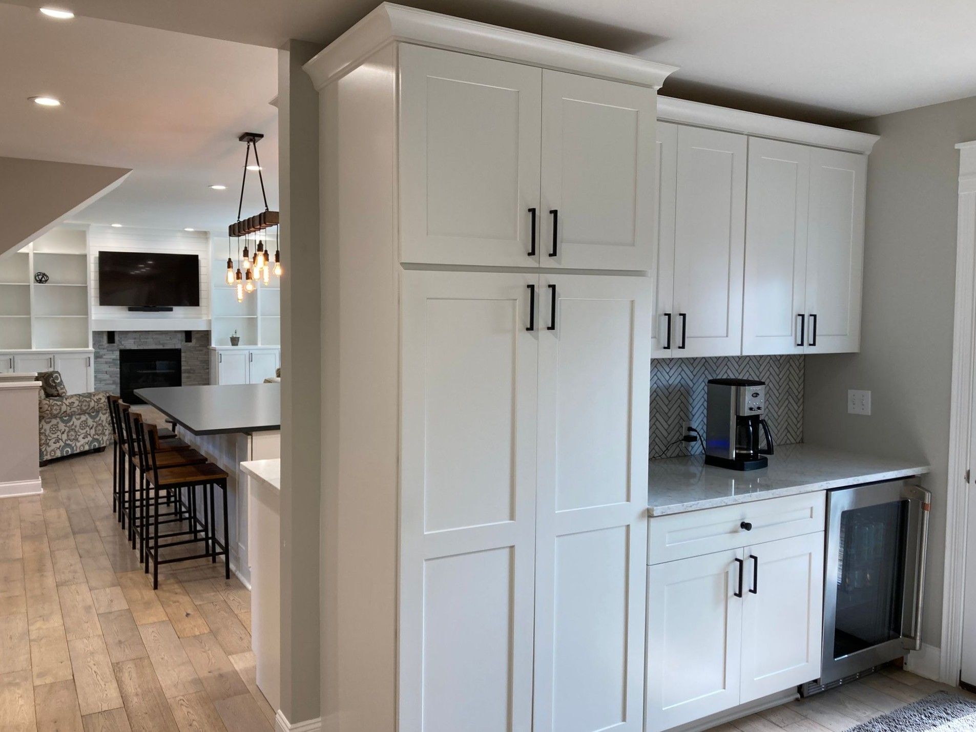 Modern white kitchen with island seating, built-in cabinets, and stainless appliances opening to a living area