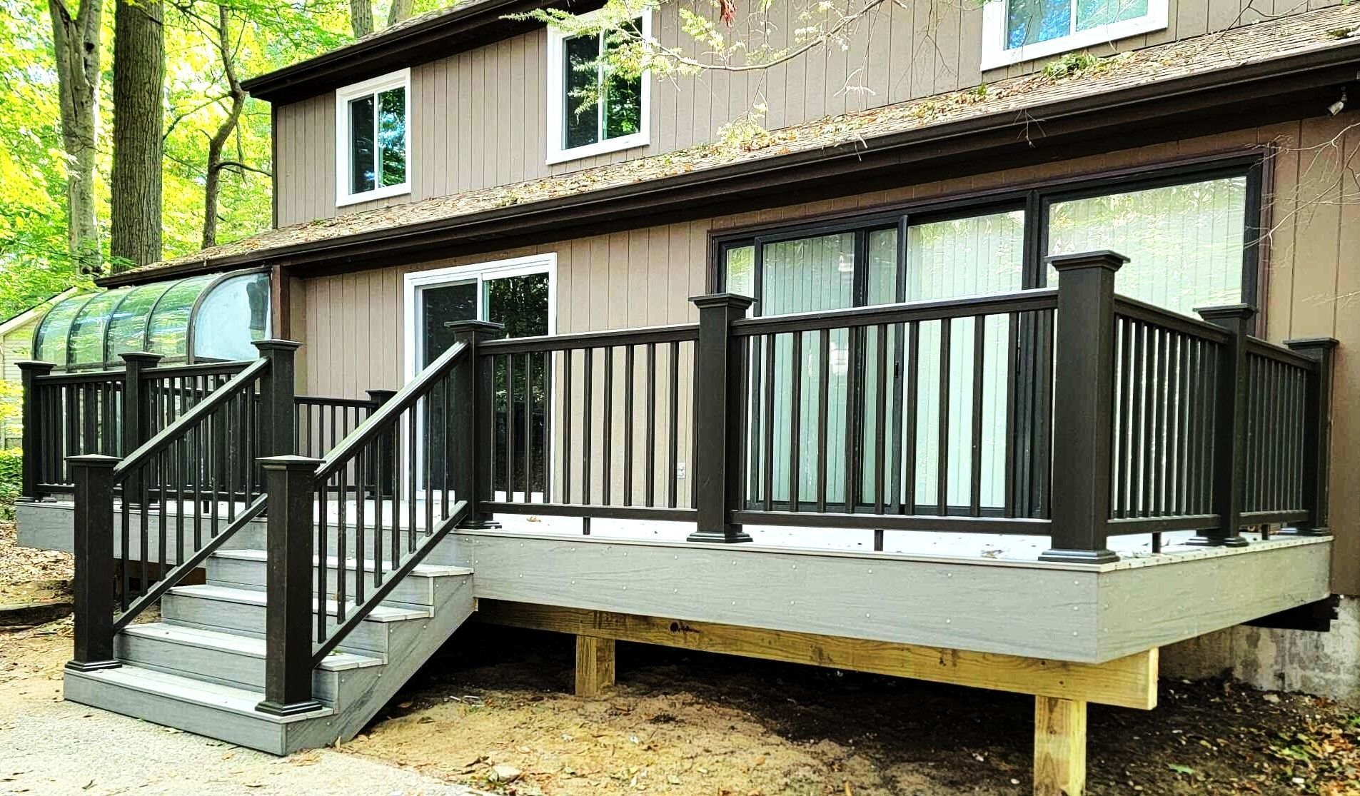 Wooden deck with black railings attached to a house in a wooded area.