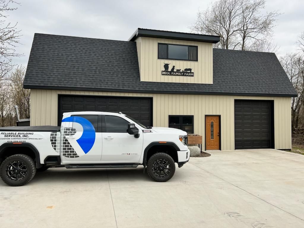White work truck parked in front of a beige building with a black roof and garage door.