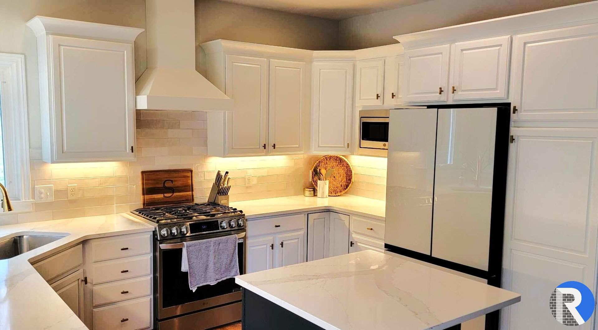 Bright white kitchen with cabinets, gas stove, refrigerator, and a central island under warm lighting