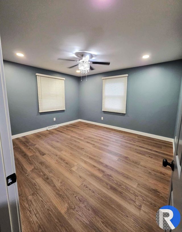 Empty gray bedroom with wood floor, two windows, white trim, and a ceiling fan.