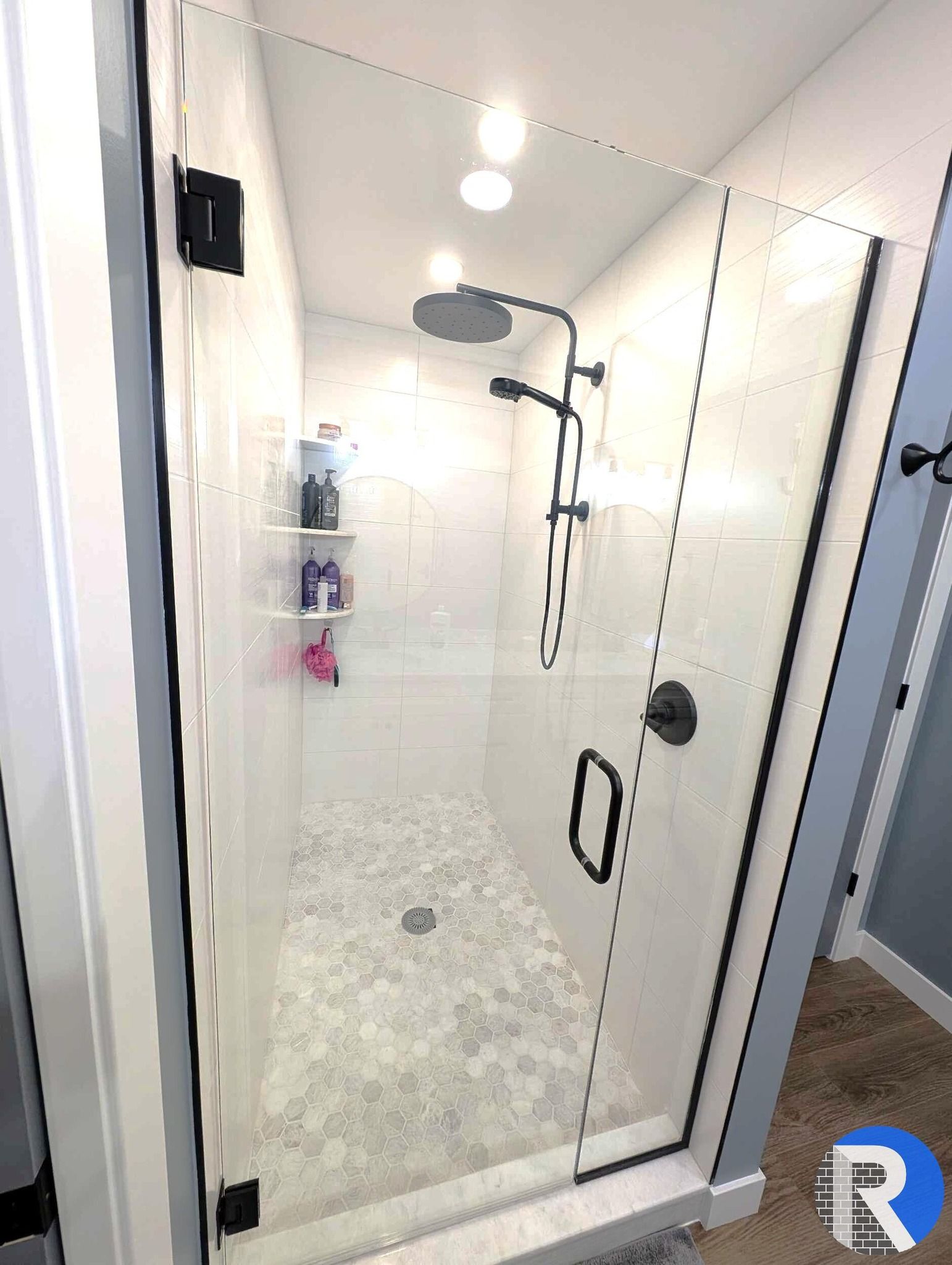Glass shower enclosure with black hardware in a bright tiled bathroom