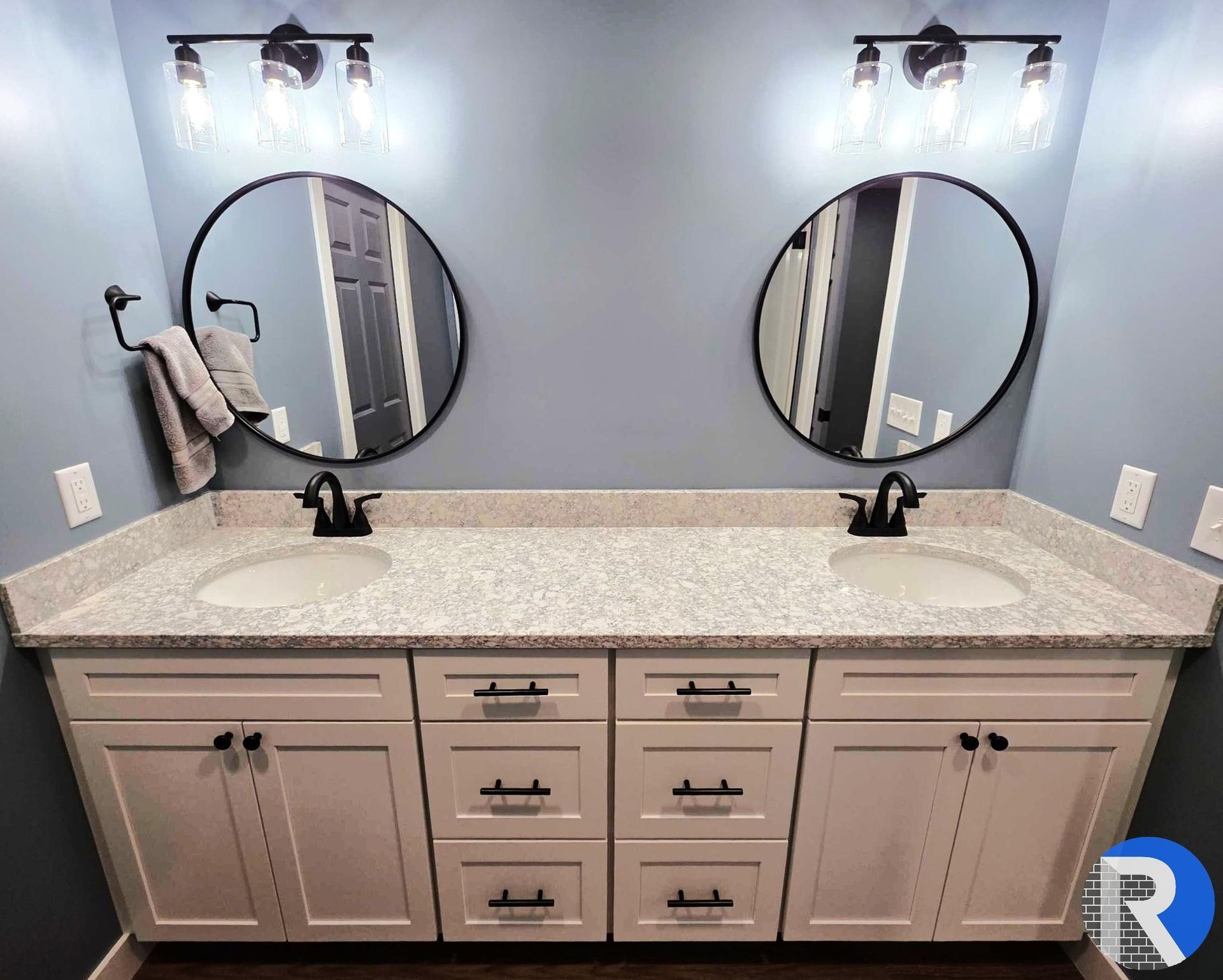 Double vanity bathroom with two round mirrors, white countertop, and gray cabinets under wall lights