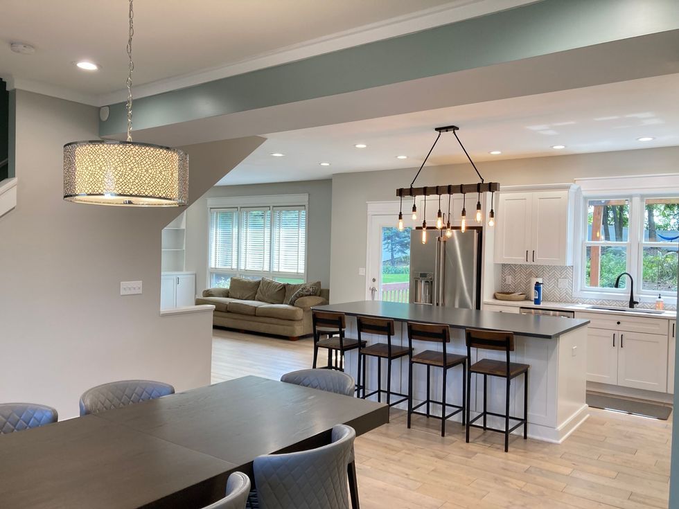 Bright open kitchen and dining area with island seating, stainless fridge, pendant lights, and large windows