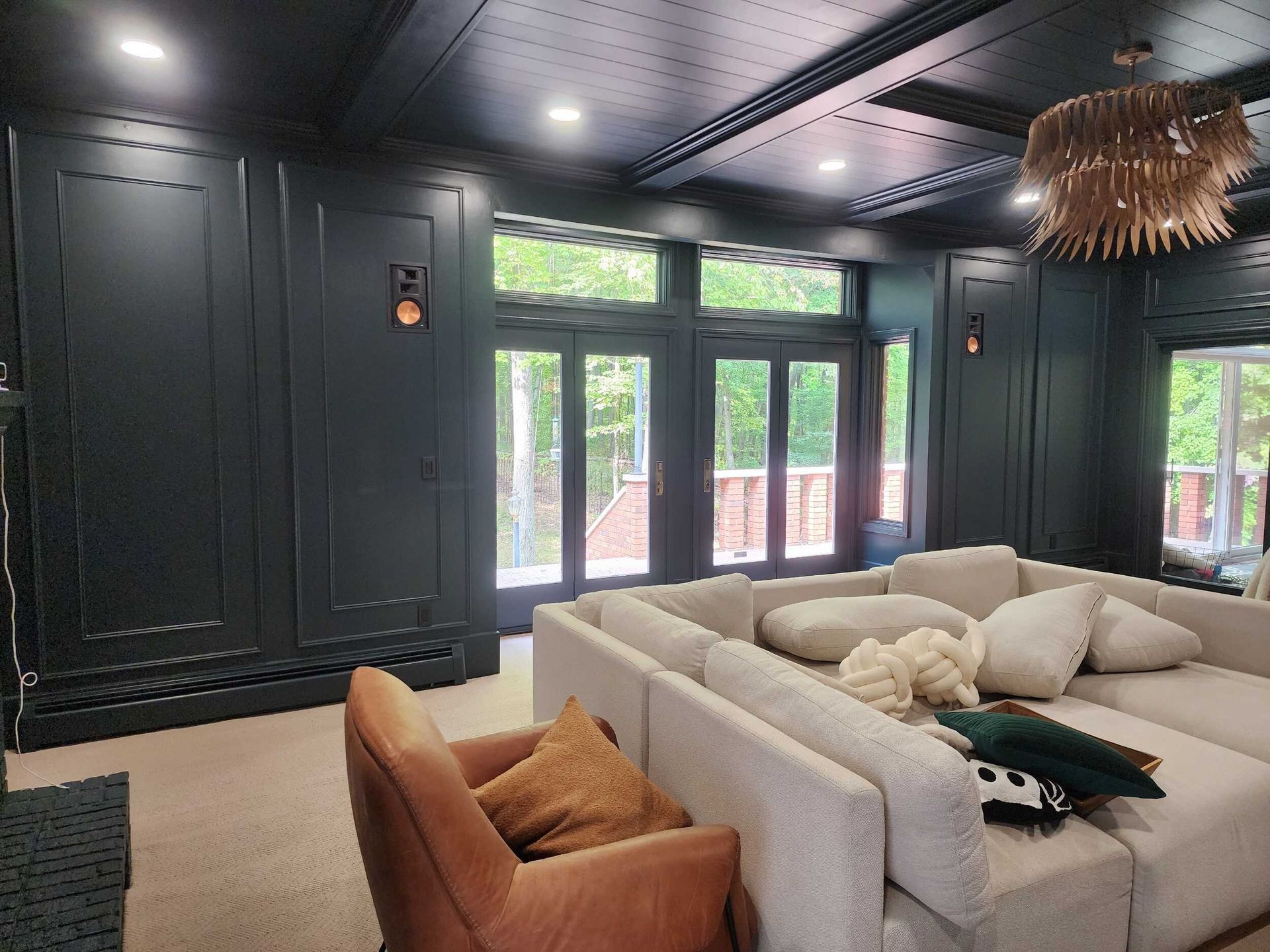 Modern living room with black paneled walls, beige sectional sofa, and large windows letting in natural light