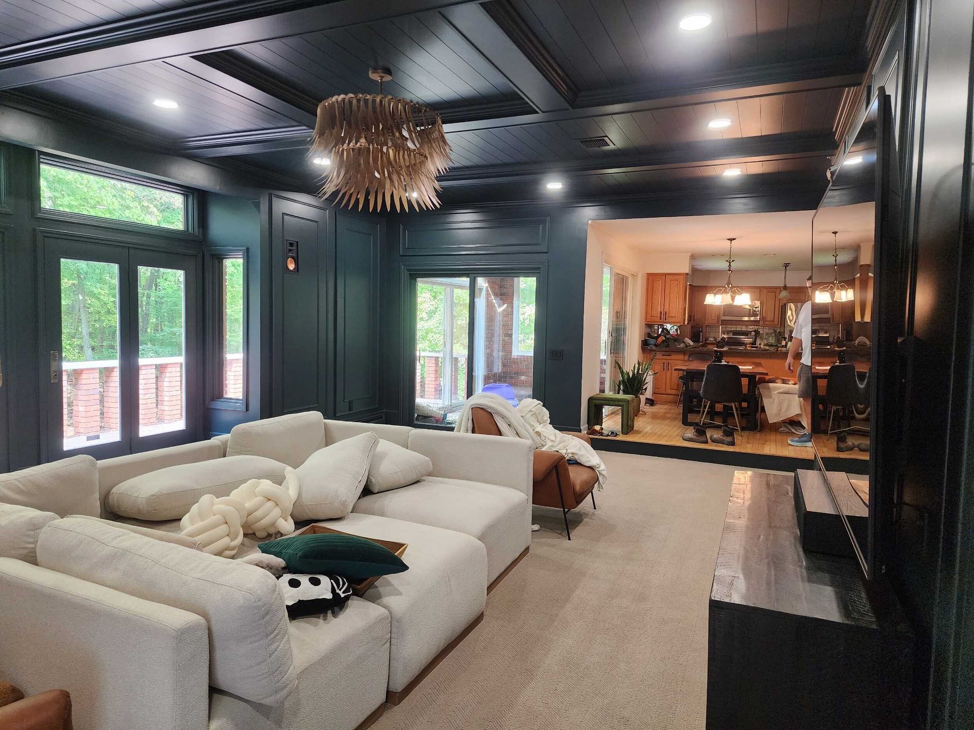 Modern living room with white sectional, dark ceiling, large windows, and a glimpse of a dining area beyond.