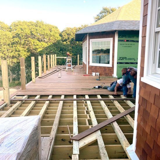 Workers installing a wooden deck beside a house, with exposed joists in the foreground.