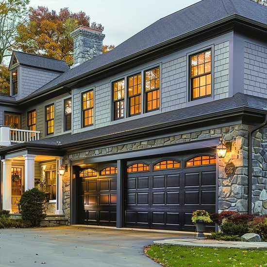Elegant gray two-story house with lit windows, stone accents, and a dark double garage at dusk