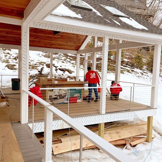 Two workers in red jackets building a white porch on a snowy hillside