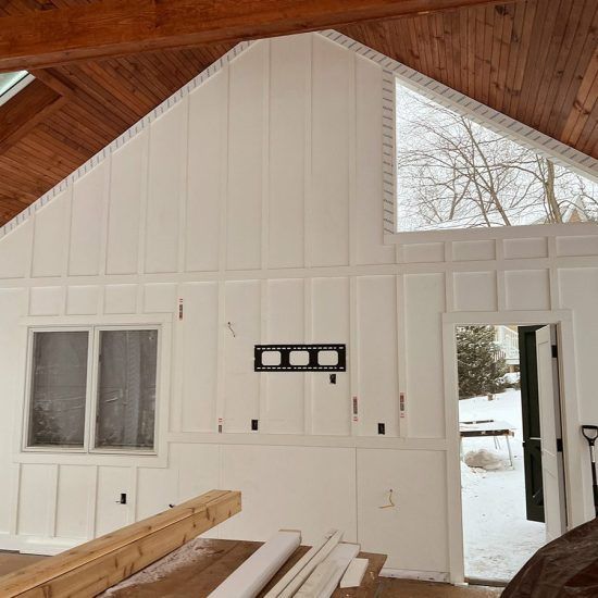Interior of a white barn-like room with wood ceiling, windows, open door, and construction materials inside