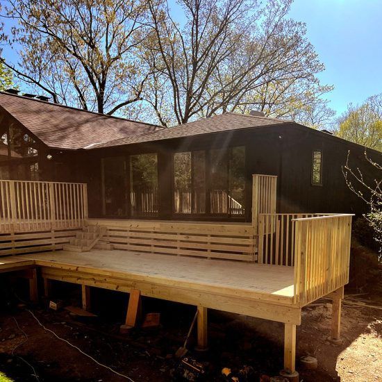 Wooden deck beside a dark brown house under leafless trees on a sunny day