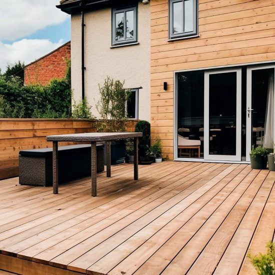Wooden patio deck with outdoor table and seating beside a modern house with sliding glass doors