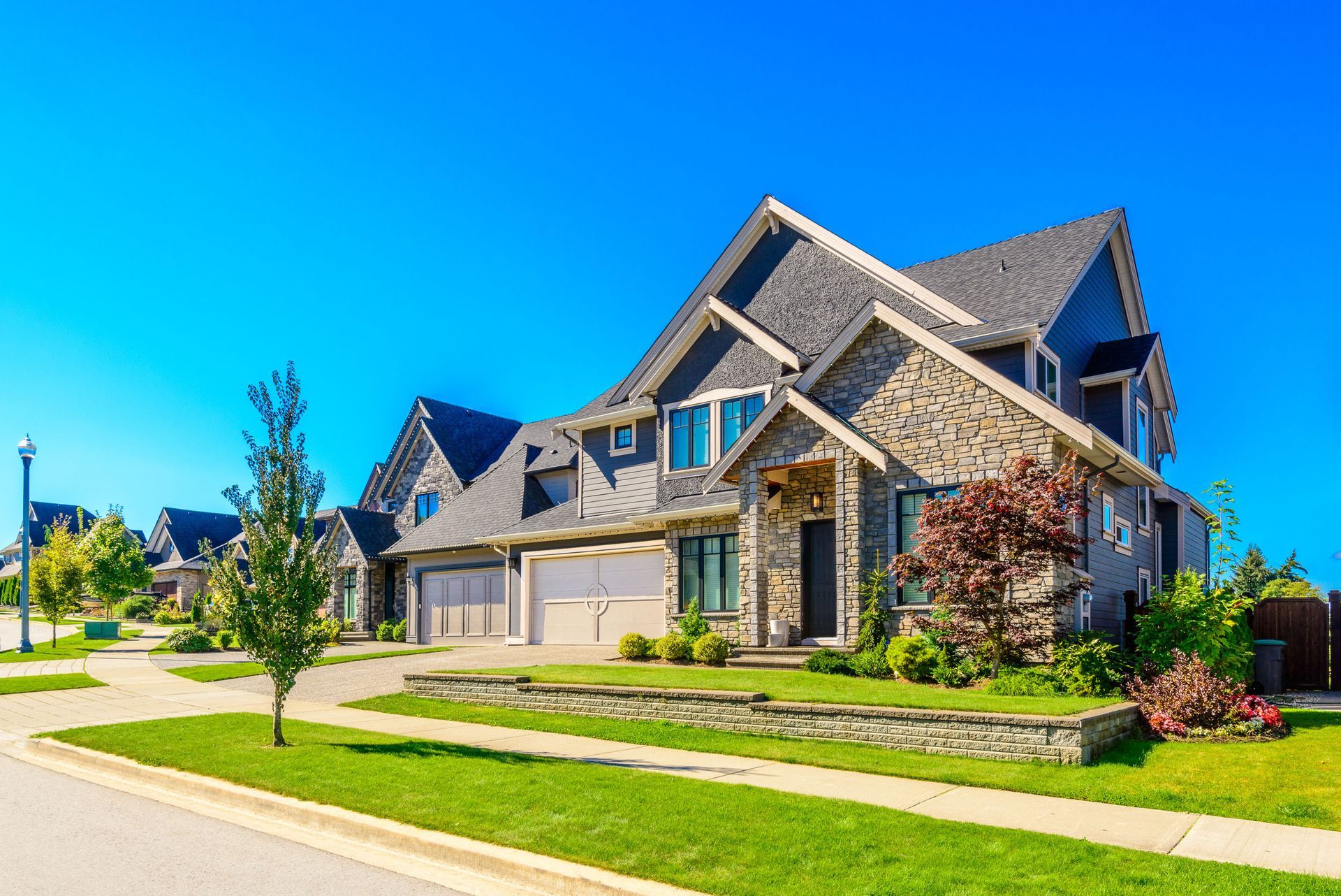 Modern stone suburban house with manicured lawn, driveway, and bright blue sky