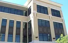 Office building with tan brick facade, large windows, and a clear blue sky.