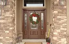 Brown front door with wreath, flanked by stone columns; a shovel leans against the right side.