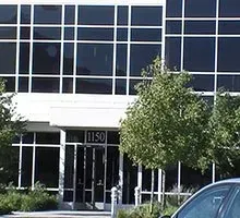 Office building with large windows; entrance marked 1150; a tree is in front.