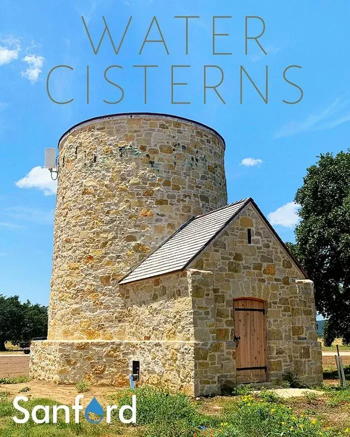 Stone water cistern building with a cylindrical tower and gabled roof, blue sky backdrop.