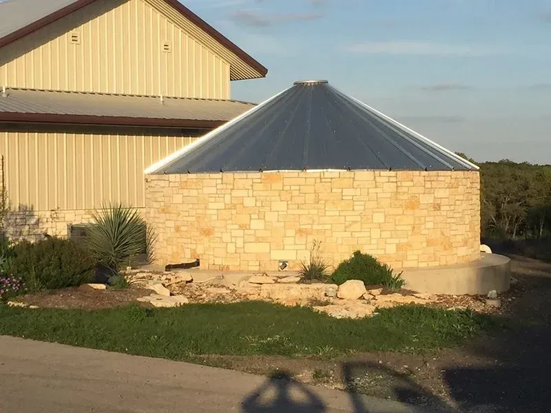 Stone silo with a translucent angled roof, next to a building.