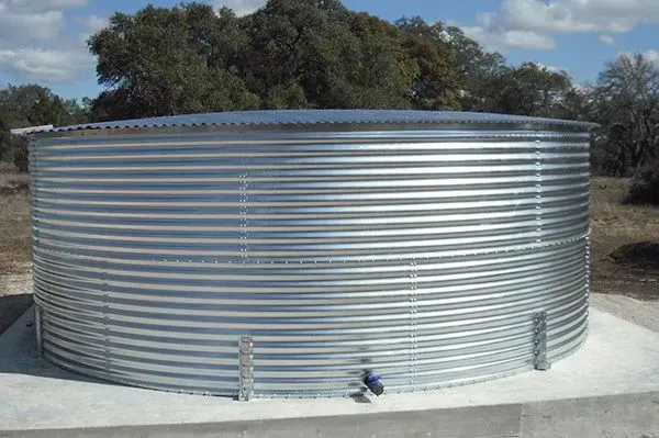 Large, corrugated metal water storage tank on a concrete base, outdoors under a sunny sky.