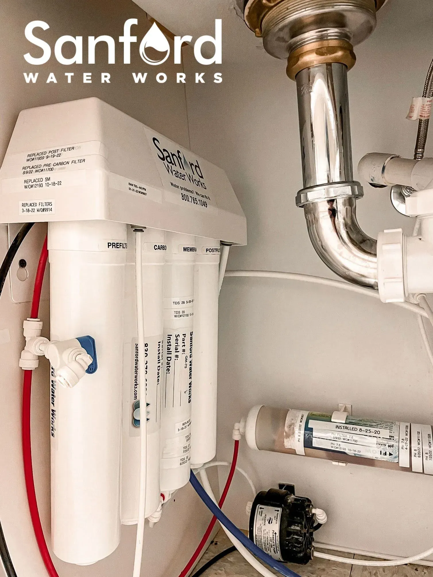 Water filter system installed under a sink. White filter canisters with red and blue tubes. 