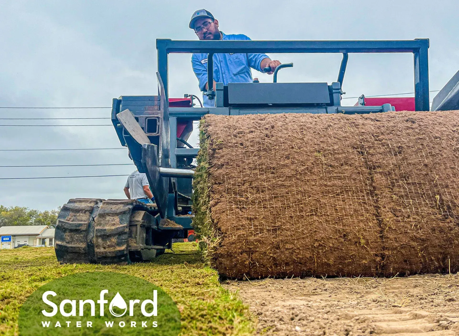 A worker operating sod harvester, rolling a section of turf. Sanford Water Works logo.
