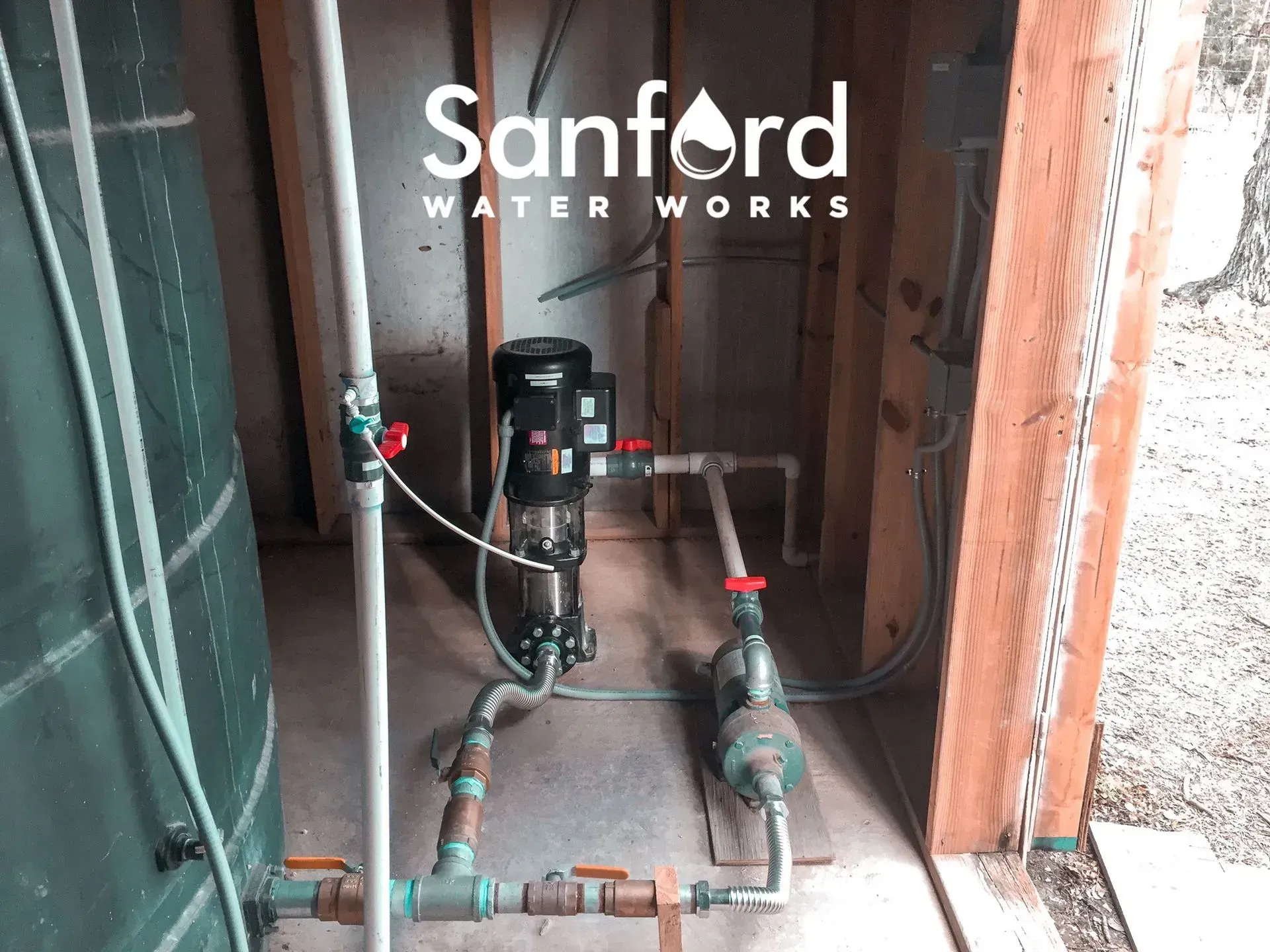Water pump system with pipes and valves, installed in a wooden framed structure. 