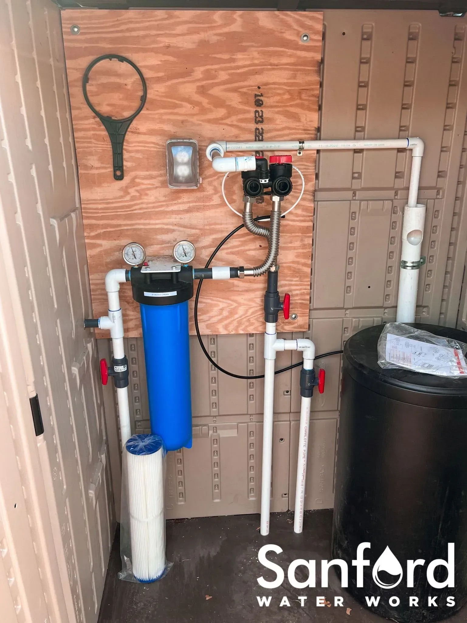 Water filtration system with blue filter, black tank, PVC pipes, and a wrench.